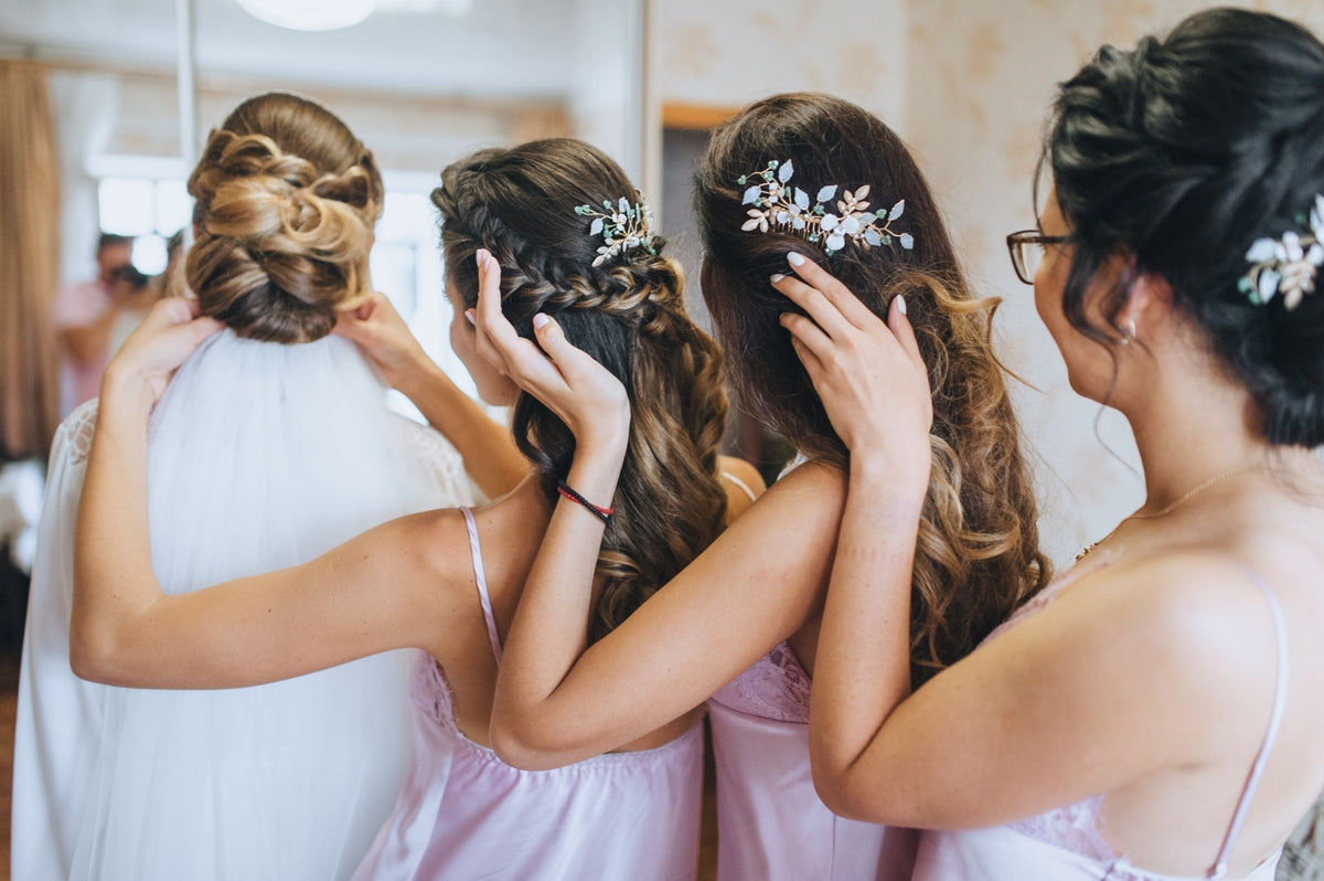 Bridesmaids helping a bride adjust her veil, showcasing their intricate hairstyles and hair accessories.